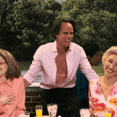 a man without a shirt is smiling while sitting at a table with other people