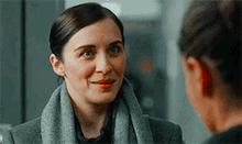 a woman wearing a scarf and a coat is smiling at another woman .