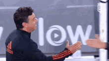 a man in a black adidas jacket is giving a high five to another man in front of a sign that says low .