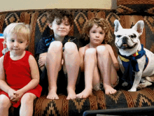 three children sit on a couch with a dog