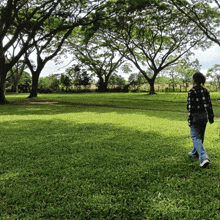a woman in a plaid shirt walks through a grassy field