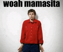 a man in a red shirt stands in front of a white wall with the words woah mamasita written above him