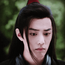 a young man with long black hair has a red ponytail on top of his head