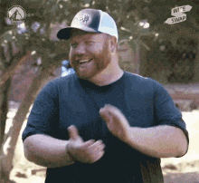 a man with a beard wearing a hat and a black shirt is clapping .