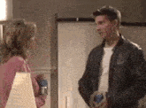 a man in a leather jacket is talking to a woman in a pink shirt