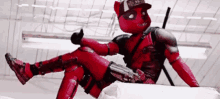 deadpool is giving a thumbs up while sitting on a bed .