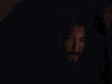 a man with long hair and a mustache is looking down in the dark .
