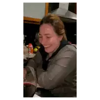 a woman covering her face with her hand while sitting in a kitchen