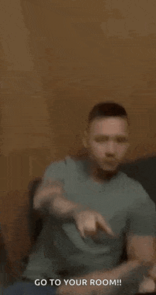 a man is pointing at the camera while sitting on a couch and saying `` go to your room '' .