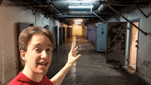 a man in a red shirt is standing in a dark hallway and pointing