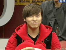 a man in a red jacket is smiling in front of a sign that says sina on it