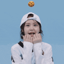 a girl wearing a baseball cap is holding her hands to her face while a cookie is flying in the air