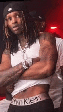 a man with dreadlocks is standing with his arms crossed in a white tank top and black underwear .