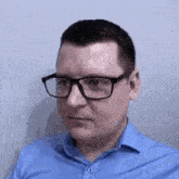 a man wearing glasses and a blue shirt is standing in front of a wall .