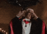 a man in a tuxedo and a red cape is holding his head .
