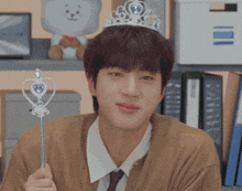 a young man wearing a tiara and holding a wand is making a funny face .