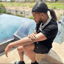 a man with a ponytail is sitting next to a swimming pool