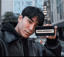 a man in a black jacket holds up a cell phone with the words open mindeu on it