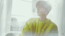 a person in a yellow sweater is sitting in front of a window with soap bubbles coming out of it .