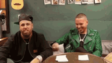 a man in a green leather jacket sits next to another man in a black jacket