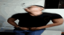 a man in a black shirt and blue jeans is standing in a room with his hands on his stomach .