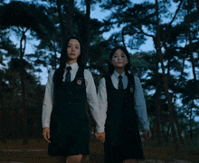 two girls in school uniforms holding hands in the woods