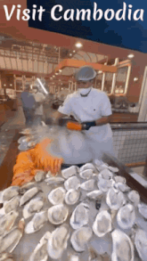 a chef prepares oysters in front of a sign that says visit cambodia on it
