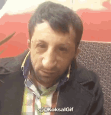 a man wearing a plaid shirt and a black jacket is sitting on a couch and making a funny face