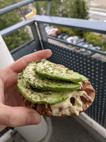 a person holding a sandwich with avocado on top