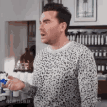 a man wearing a leopard print sweater is standing in a kitchen and making a funny face .