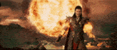 a man in a costume is standing in front of a huge fireball .