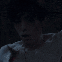 a man without a shirt is laying in a dark room with blood on his chest .