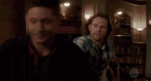 two men are standing next to each other in a room and one of them is wearing a plaid shirt .
