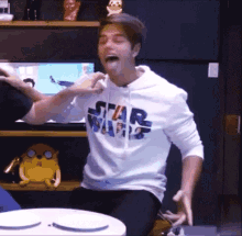 a man wearing a star wars hoodie is sitting at a table eating a piece of food .