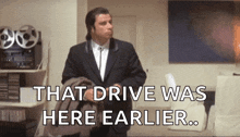 a man in a suit and tie is standing in a living room with the words `` that drive was here earlier ''