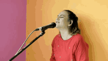 a woman singing into a microphone in front of a pink and orange wall
