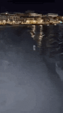 a person is walking on a beach at night with a city in the background .