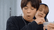two young men are sitting next to each other and one of them is eating something from a plastic container .