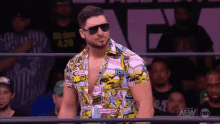 a man wearing sunglasses and a colorful shirt is standing in a wrestling ring in front of a crowd .