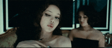 two women are sitting on a couch one is wearing a black dress and the other is wearing a white dress