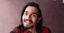 a young man with long hair and a beard is smiling .