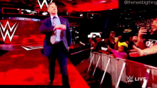 a man in a suit and tie is walking on a red carpet in front of a crowd and a wwe logo