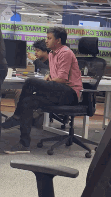 a man in a pink shirt sits in a chair in front of a sign that says ' oi9man '