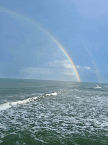 a rainbow appears over the ocean with waves crashing on the shore