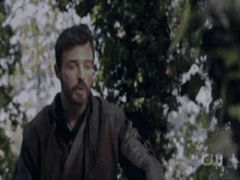 a man with a beard is standing in the woods looking at something .
