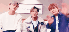three young men are sitting next to each other in a room and waving at the camera .