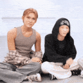 two young men sit on the floor one wearing a black hoodie that says ' i love you ' on it