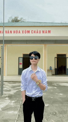 a man wearing sunglasses stands in front of a building that says " a van hoa xom chau nam " on it