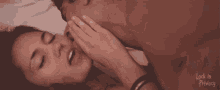 a man and a woman are kissing in bed and the woman is covering her mouth with her hand .