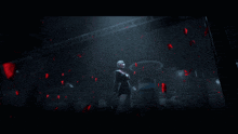 a woman in a black dress stands in a dark room surrounded by red petals